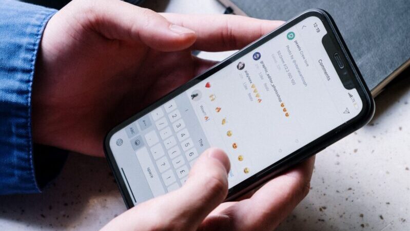 Close-up of hands holding smartphone, using chat app. Coffee and notebook nearby indicate casual setting.