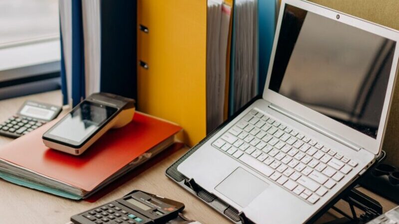 Modern workplace setup with laptop, folders, and gadgets by a window view.